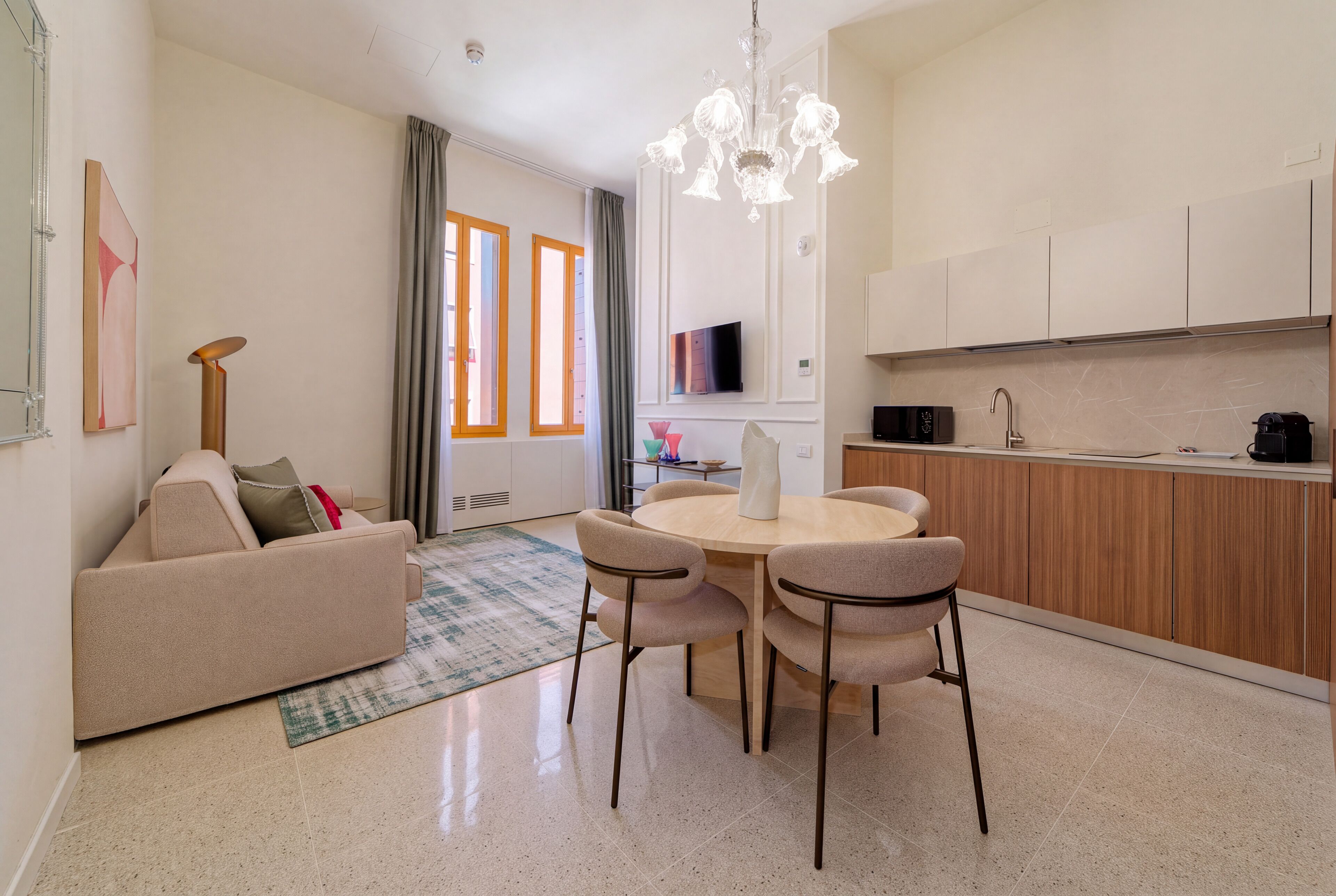 Una sala moderna con un sofá, una mesa de comedor con sillas, una cocina con armarios, y un ventanal con cortinas.