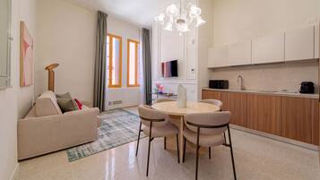 Una sala moderna con un sofá, una mesa de comedor con sillas, una cocina con armarios, y un ventanal con cortinas.