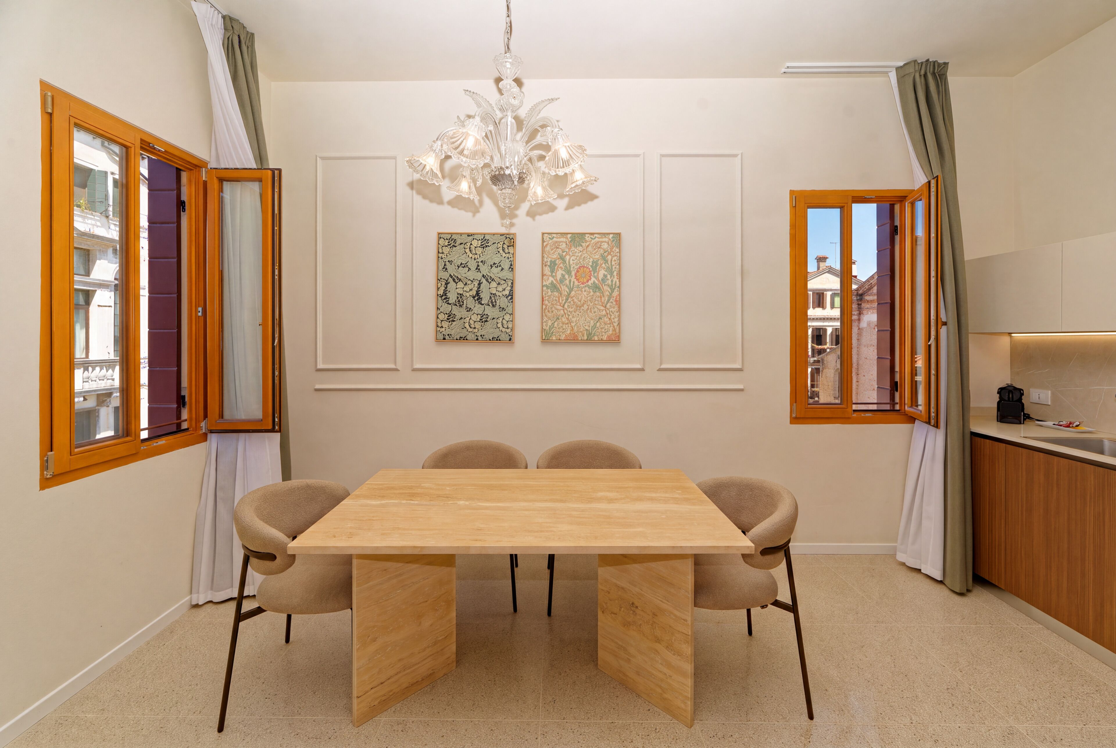 A dining room with a wooden table, four chairs, a chandelier, and two framed artworks on the wall.