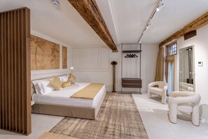 A bedroom with a large bed, a wooden headboard, a floor lamp, a wardrobe, a mirror, and a chair.