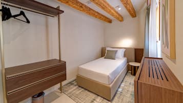 Quarto de hotel com cama, mesa de cabeceira, mesinha redonda, lixeira e cabideiro.