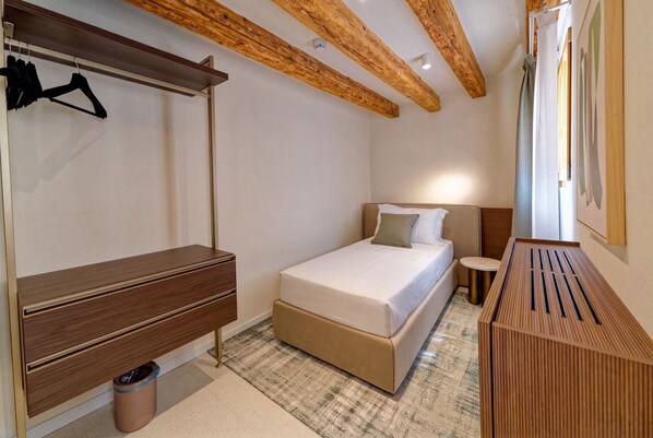 A hotel room with a bed, a bedside table, a small round table, a trash bin, and a coat rack. - Be Mate Santa Croce (Venezia)