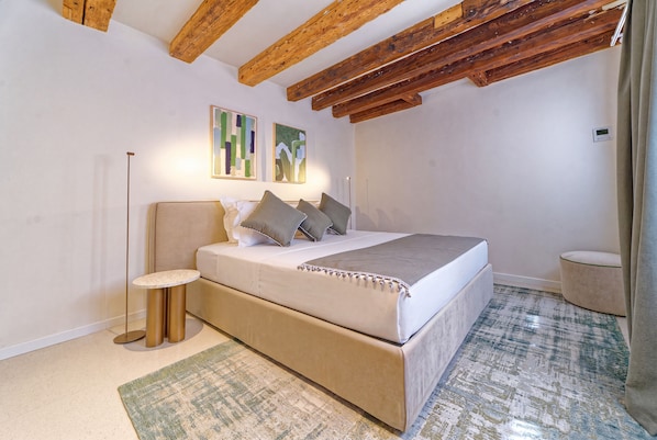 A bedroom with a bed, a bedside table, a floor lamp, and two abstract paintings on the wall. - Be Mate Santa Croce (Venezia)