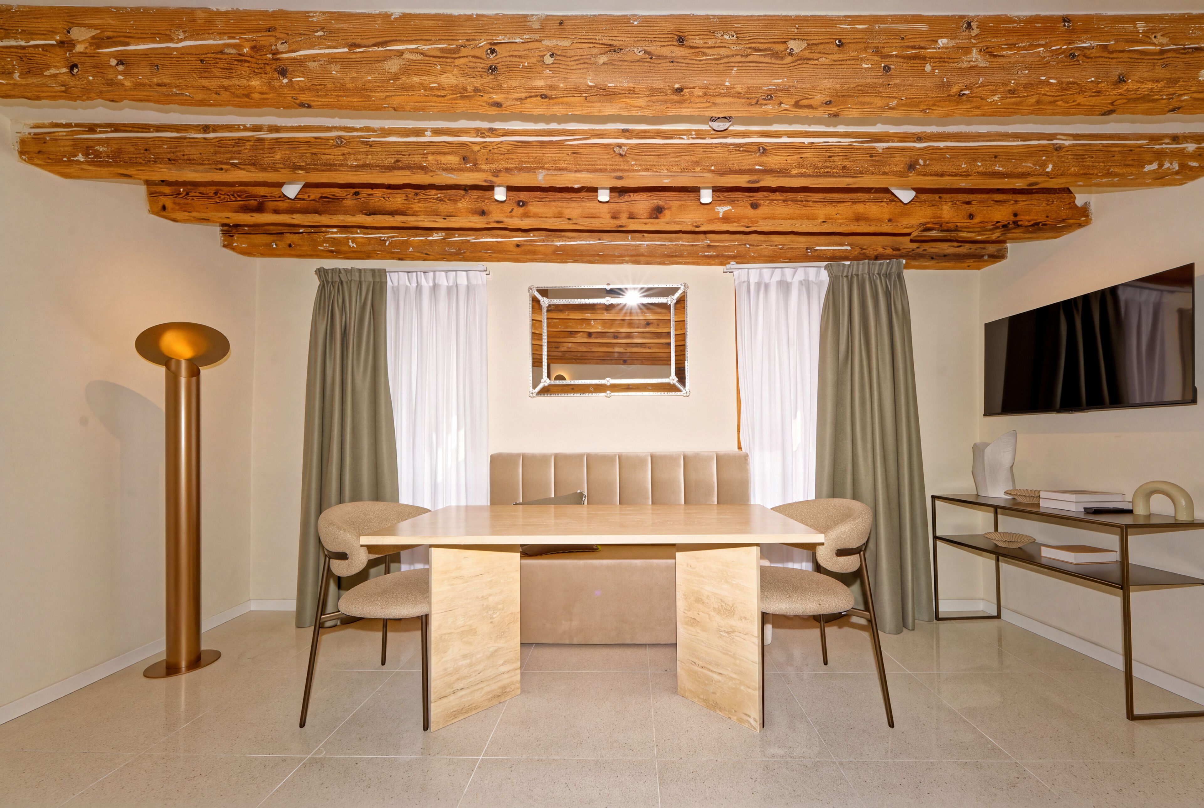 A dining area with a wooden table, two chairs, a bench, a floor lamp, and a mirror on the wall.