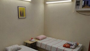 Una habitación pequeña con dos camas individuales, un escritorio, una silla y un aire acondicionado instalado en la pared.