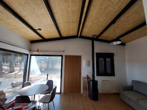 Ein Zimmer mit Holzboden, einem Esstisch mit Stühlen, einer Couch und einem großen Fenster mit Blick auf Bäume.