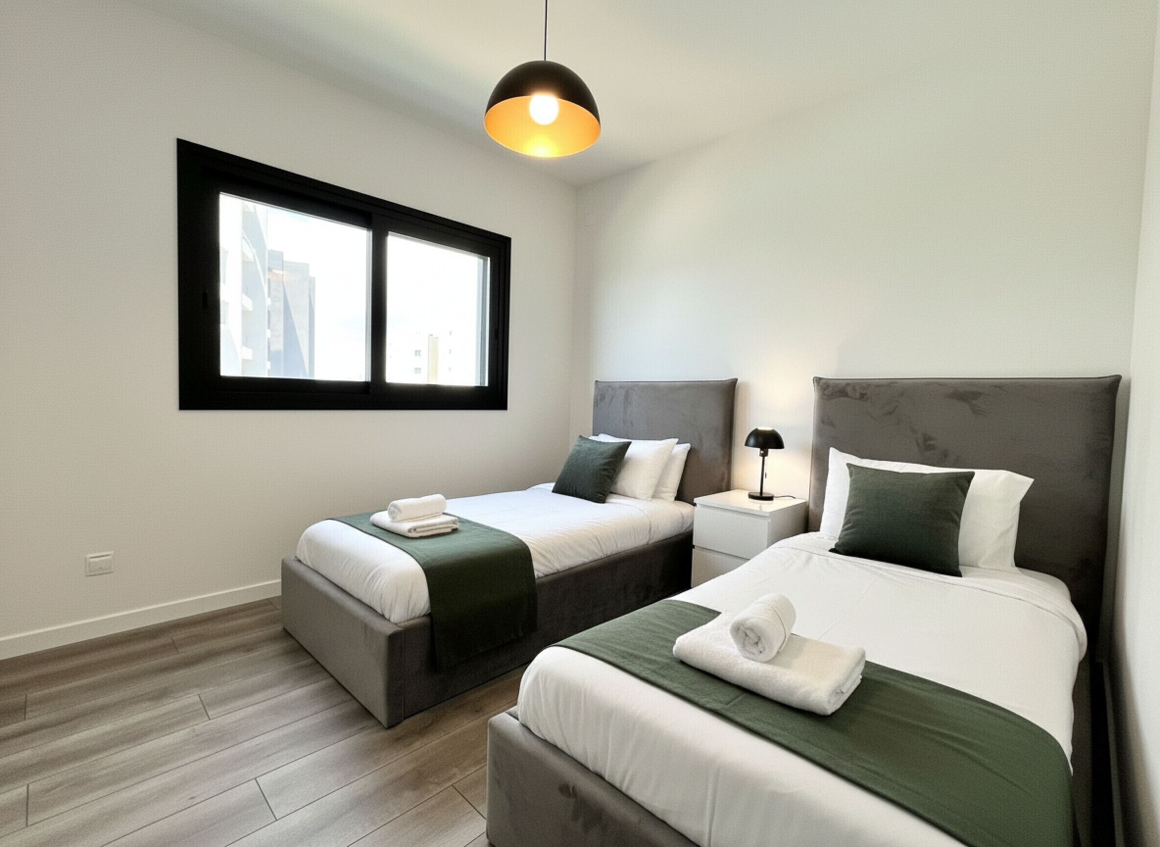 A hotel room with two beds, a window, a lamp, and a city view.