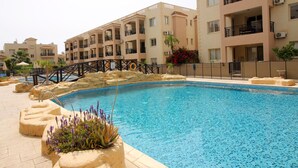 Une piscine avec un pont, entourée d’immeubles à plusieurs étages dotés de balcons et de climatiseurs.