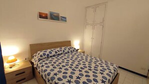 A bedroom with a bed, nightstand, lamp, wardrobe, and three wall-mounted pictures. - Otta's House (Platamona)