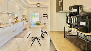 A modern kitchen with white cabinets, a dining table with chairs, a coffee machine, and a view of the outdoors. - Villa La Bella Sofia with private pool (Roda)