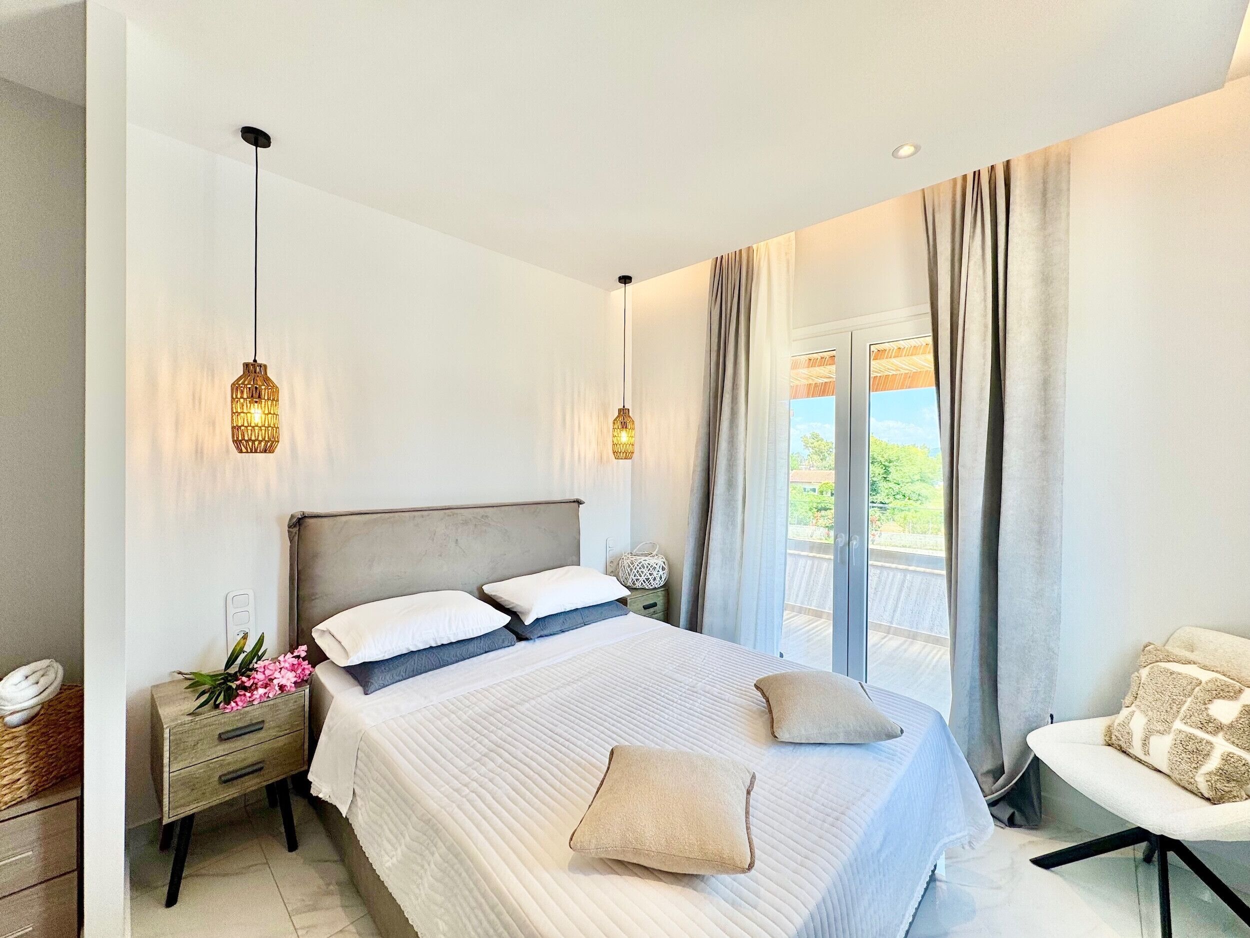 A modern bedroom with a large bed, bedside tables, a chair, and a balcony with curtains.
