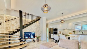 A modern living room with a stone staircase, a flat-screen TV, a dining area, and a kitchen. - Villa La Bella Sofia with private pool (Roda)