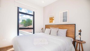 Ein Schlafzimmer mit einem großen Bett, einem Fenster und einem Nachttisch mit einer Lampe.