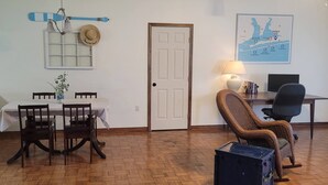 Uma área de refeições com mesa, cadeiras, uma luminária, um mapa na parede e uma porta.