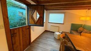A cozy room with a wooden ceiling, a dining table, a sofa, and a window with blinds. - Inlandsis Aparts (El Chalten)