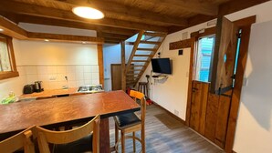A kitchen with a wooden table, chairs, a stove, and a TV mounted on the wall. - Inlandsis Aparts (El Chalten)