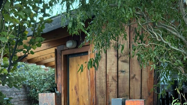 A wooden fence with vertical slats, a wooden door, and a wooden structure with a sloped roof. - Inlandsis Aparts (El Chalten)