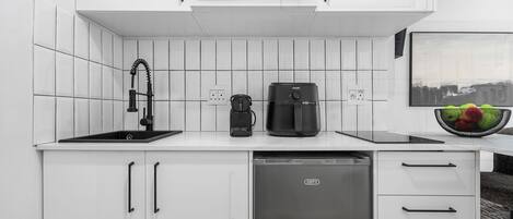 Une cuisine moderne avec des meubles blancs, une machine à café noire, un four à micro-ondes noir et un lave-vaisselle.