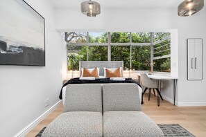 A modern bedroom with a large window, a bed with patterned bedding, a desk, and a chair. - Modern Green Point Studio Walk to Promenade (Cape Town)