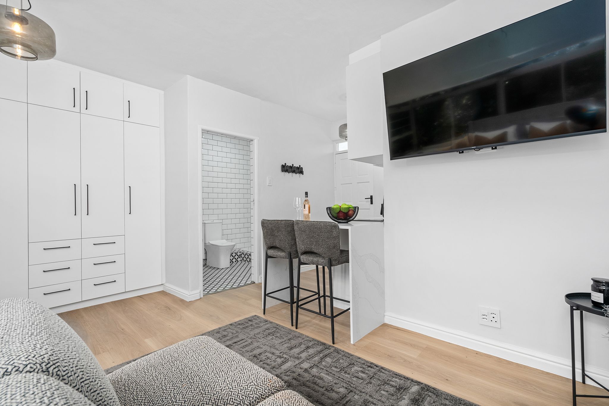 A modern kitchen with white cabinets, a bar stool, and a TV mounted on the wall.