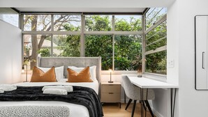 Un dormitorio con un ventanal grande, una cama, un escritorio y una silla.