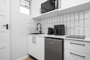 A modern kitchen with white cabinetry, a black coffee maker, a black microwave, and a dishwasher. - Modern Green Point Studio Walk to Promenade (Cape Town)