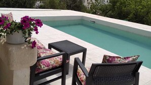 A rooftop pool area with two chairs and a table, surrounded by greenery and buildings. - Villa Marica (Ostuni)