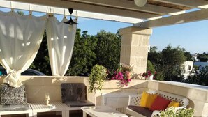A covered outdoor seating area with a table, chairs, and a decorative vase. - Villa Marica (Ostuni)