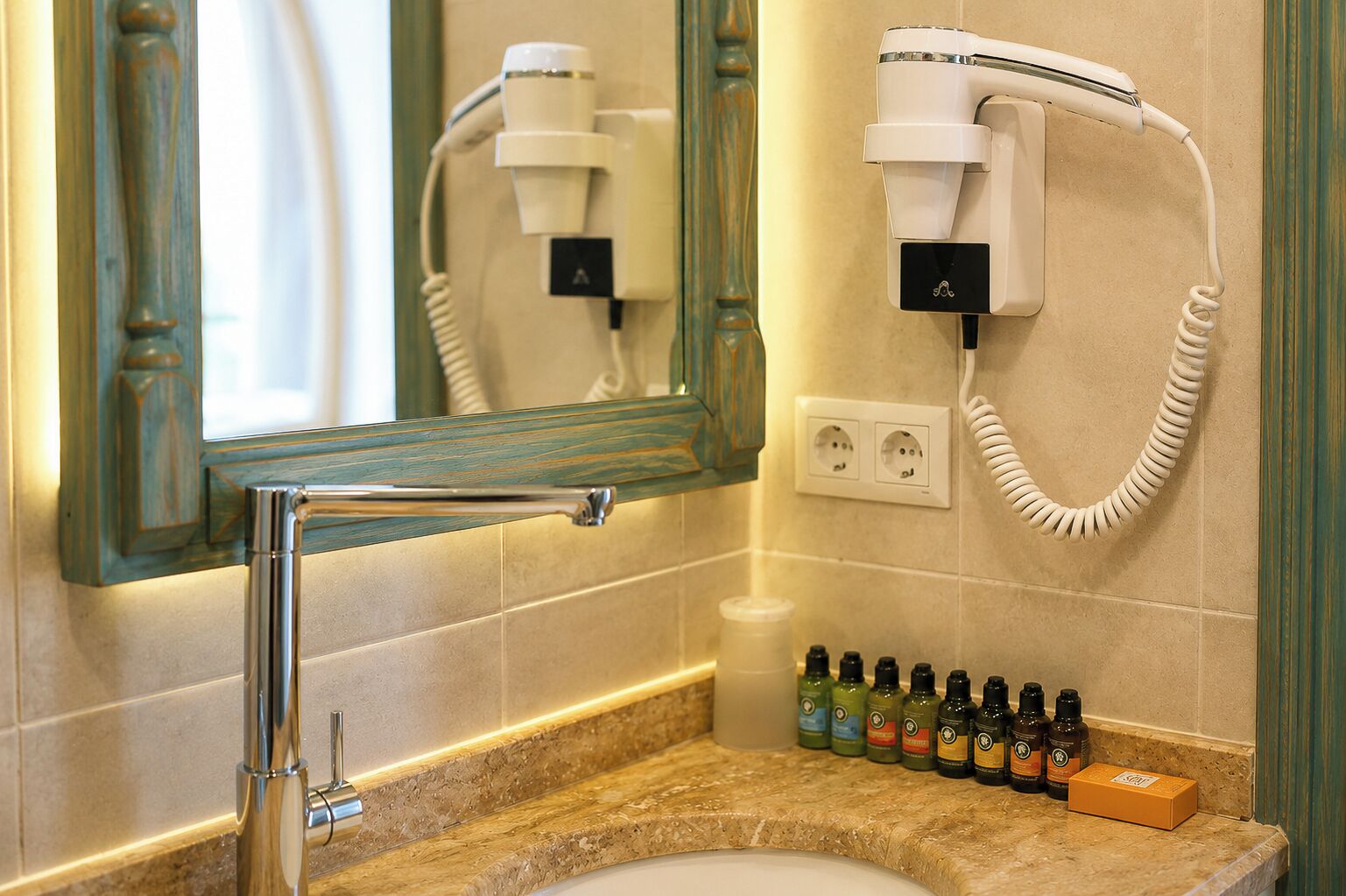 Casa de banho com secador de cabelo, espelho, lavatório e uma seleção de produtos de higiene pessoal.