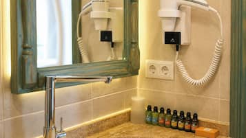 Casa de banho com secador de cabelo, espelho, lavatório e uma seleção de produtos de higiene pessoal.