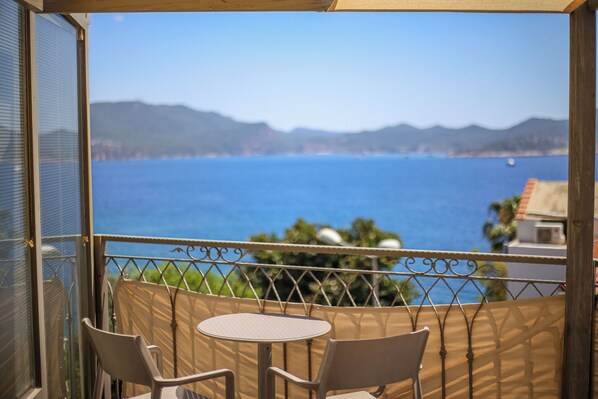 A balcony with a table and chairs, overlooking a coastal view with mountains and the sea.