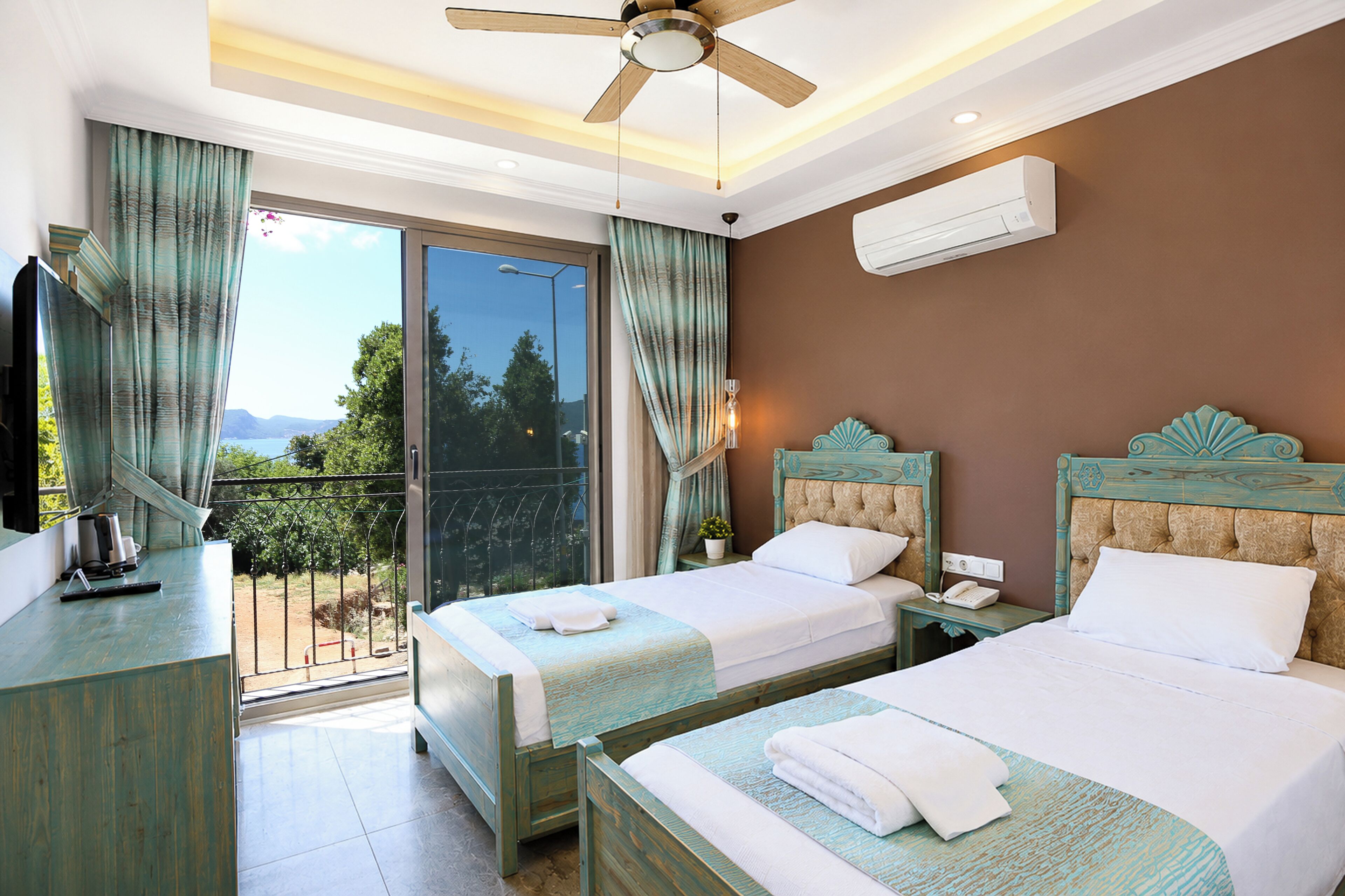 A hotel room with two beds, a balcony with a view, a ceiling fan, and an air conditioning unit.