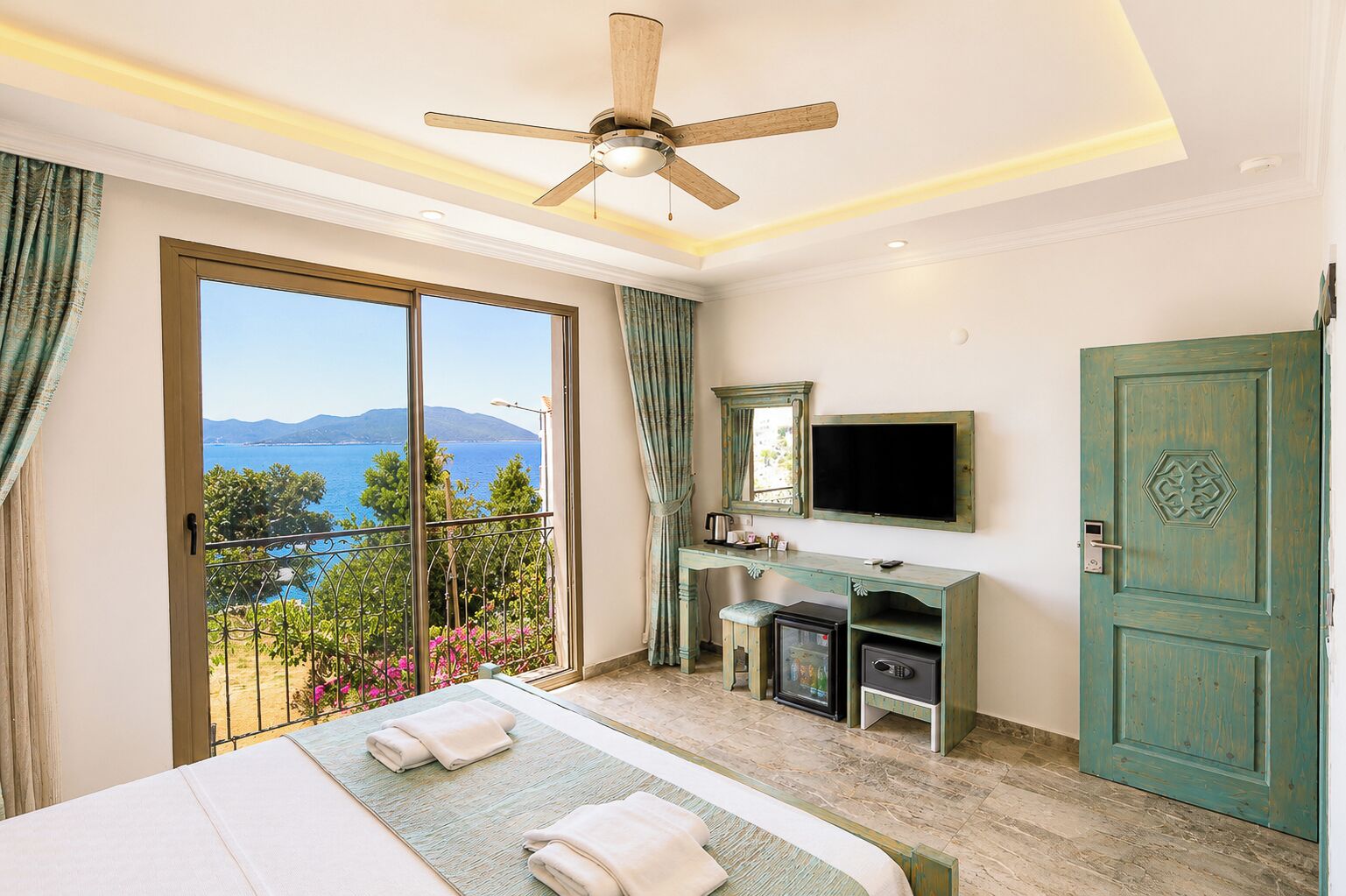 Habitación de hotel con balcón, cama, escritorio con televisor y armario.