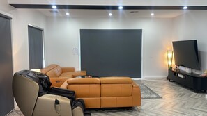 Een moderne woonkamer met een hoekbank, een flatscreen televisie en een kleine tafel met een lamp.