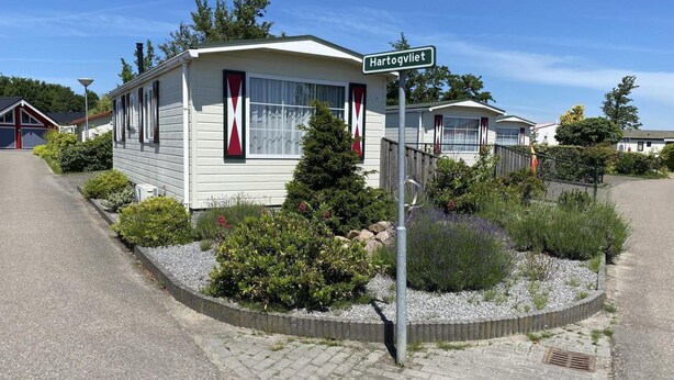 A mobile home with a flag on the window, a street sign reading 'Hartogvliet,' and a gravel garden with various plants. - Waterview Chalet Near Marina Beach (Sint-Annaland)