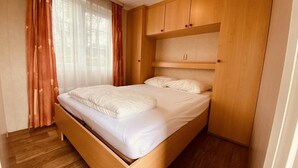 A single bed with a wooden headboard, a wooden floor, and a window with sheer curtains. - Waterview Chalet Near Marina Beach (Sint-Annaland)