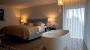 A bedroom with a large bed, bedside lamps, a bathtub, and a view of the outside through sheer curtains. - Quinta Tapada do Vale - Wine Estate Retreat (Carregal do Sal)