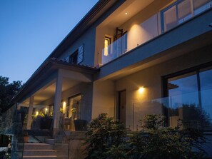 Ett modernt hus i två våningar med en inglasad veranda, stora fönster och en väl upplyst entré.