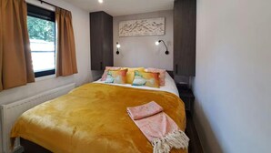 Een slaapkamer met een bed, een raam met gordijnen, een wandlamp en een radiator.