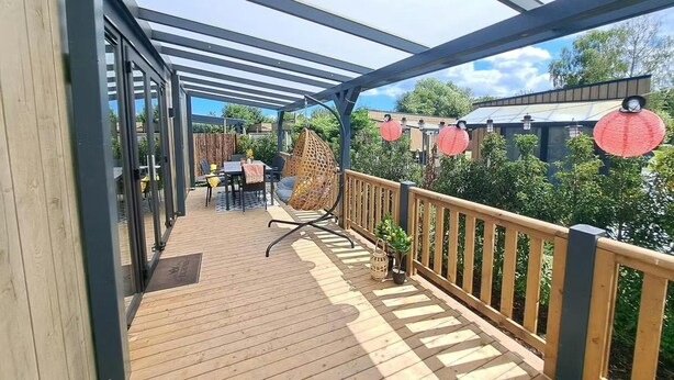 Een houten terras met een pergola, tuinmeubilair en hanglampen.