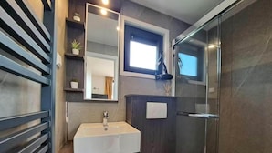 Een moderne badkamer met een inbouwwastaf, toilet, douchecabine en spiegel.
