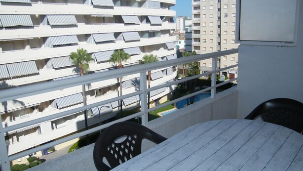 Un balcón con mesa y sillas, con vista a una piscina y edificios cercanos.
