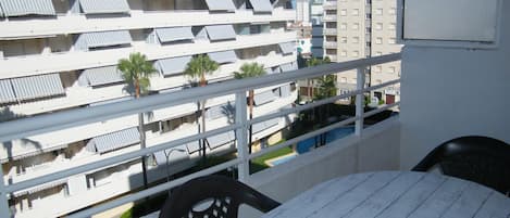 A balcony with a table and chairs, overlooking a pool and adjacent buildings.