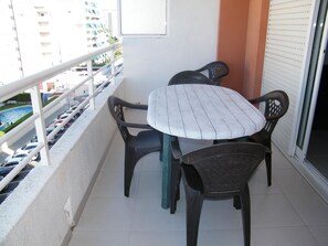 A balcony with a table and chairs, a railing, and a view of a swimming pool and buildings. - Spacious apartment with pool and parking - 6 guests (Gandia)