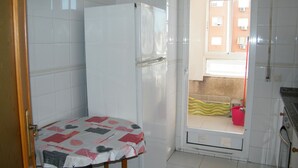 Una cocina pequeña con azulejos blancos, un refrigerador, un lavamanos y una puerta que da a un balcón.
