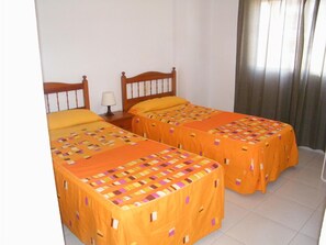 Une chambre avec deux lits, chacun doté d’une tête de lit en bois et d’une couvre-lit à motifs. Une table de chevet avec une lampe se trouve entre les deux lits.