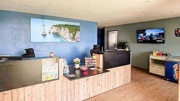 A reception desk with a wooden finish, a framed picture of a coastal scene, a television screen, and a vending machine. - Practical mobile home, pets welcome - 4 guests (Biville-sur-Mer)