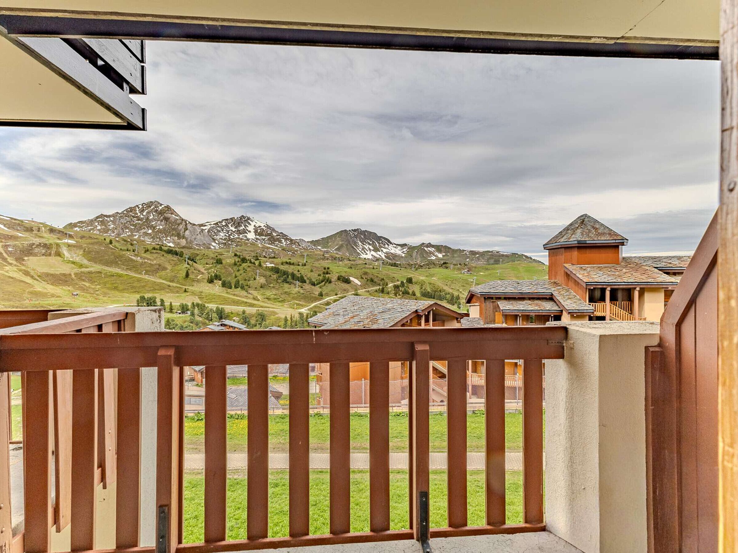 A balcony with a view of mountains and a small building with a sloped roof.