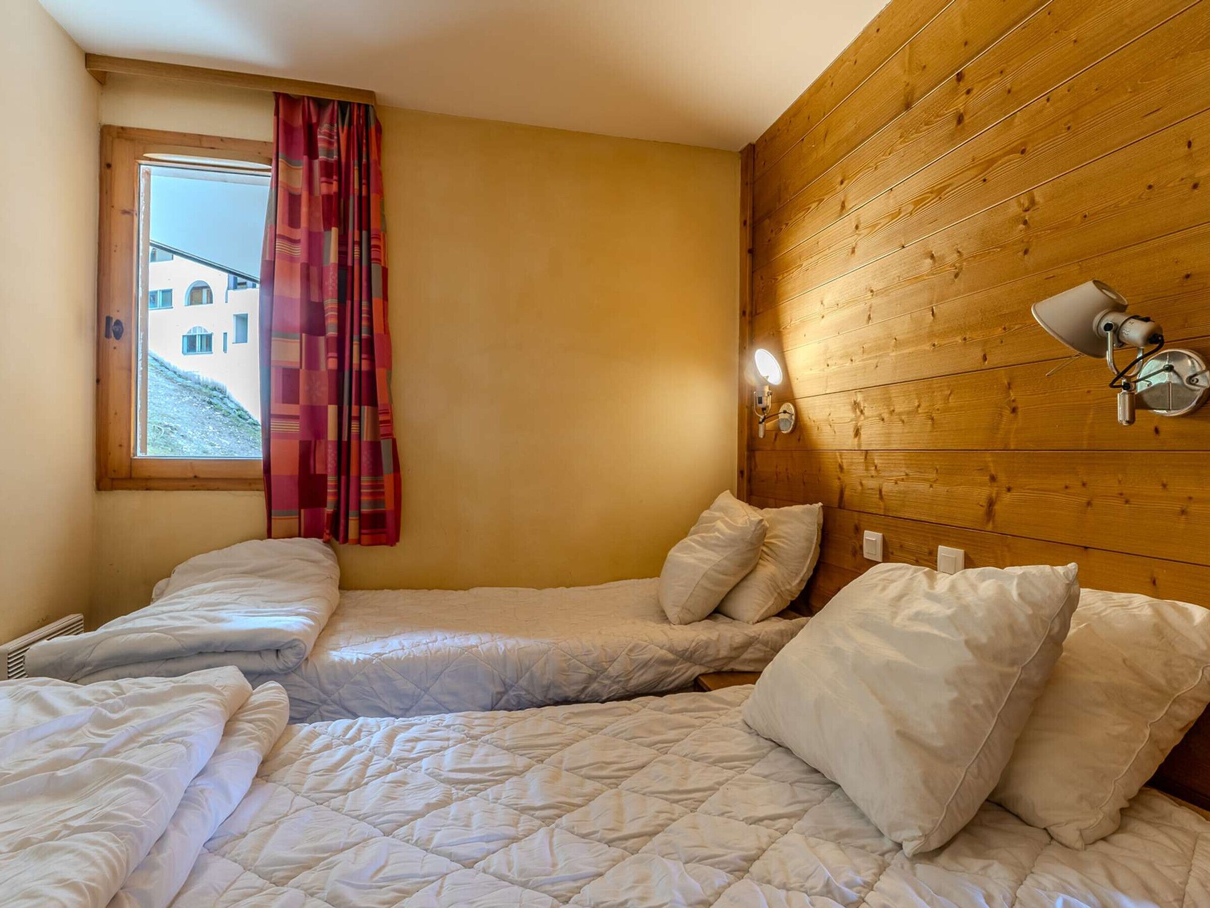 Une chambre avec deux lits, des murs en bois, une fenêtre avec des rideaux et une lampe fixée au mur.