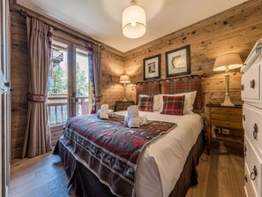 A wooden-paneled bedroom with a bed, two bedside lamps, a dresser, and a window with curtains. - Apartment chalet, relaxation - 10 guests (Courchevel)